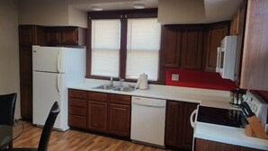 A compact kitchen with wooden cabinets, a white refrigerator, a dishwasher, and a stove. - Comfy bungalow (Carthage)