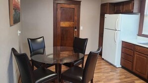A dining area with a round table and four chairs, a wooden door, a white refrigerator, and wooden cabinets. - Comfy bungalow (Carthage)