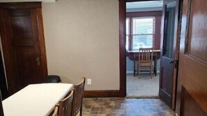 A room with a dining table and chairs, a stone floor, and a view through an open door to another room with a piano. - Cozy upstairs bungalow (Carthage)