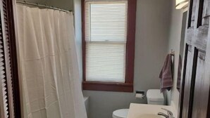 A bathroom with a shower curtain, toilet, and sink. - Cozy upstairs bungalow (Carthage)