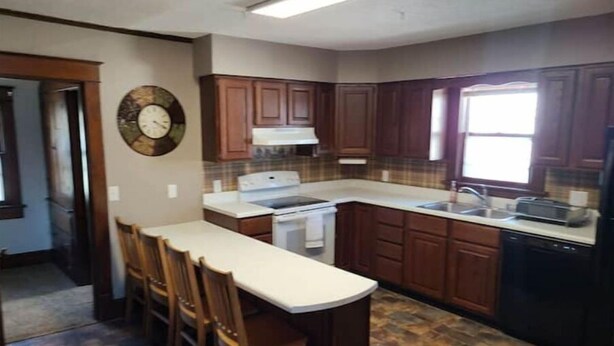 A kitchen with a central island, wooden cabinets, a stove, and a sink. - Cozy upstairs bungalow (Carthage)