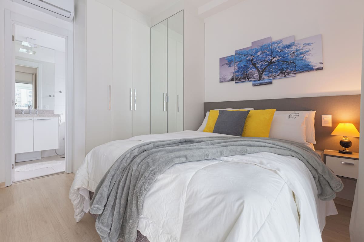 A bedroom with a bed, a nightstand, a lamp, a wardrobe, and a painting on the wall.