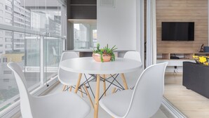 Una sala de estar moderna con una mesa redonda blanca, sillas blancas, un sofá gris y un televisor de pantalla plana montado en la pared.