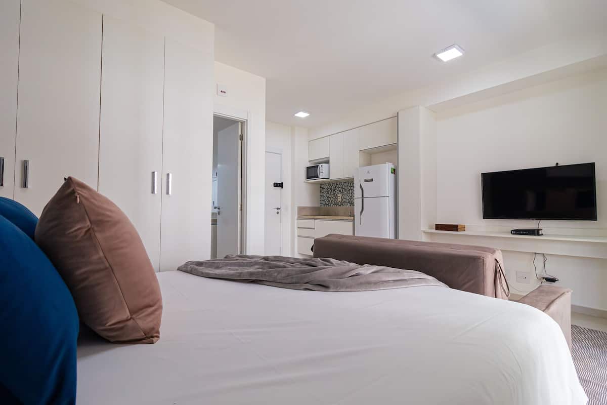 A hotel room with a bed, a television, a kitchenette, and a wardrobe.