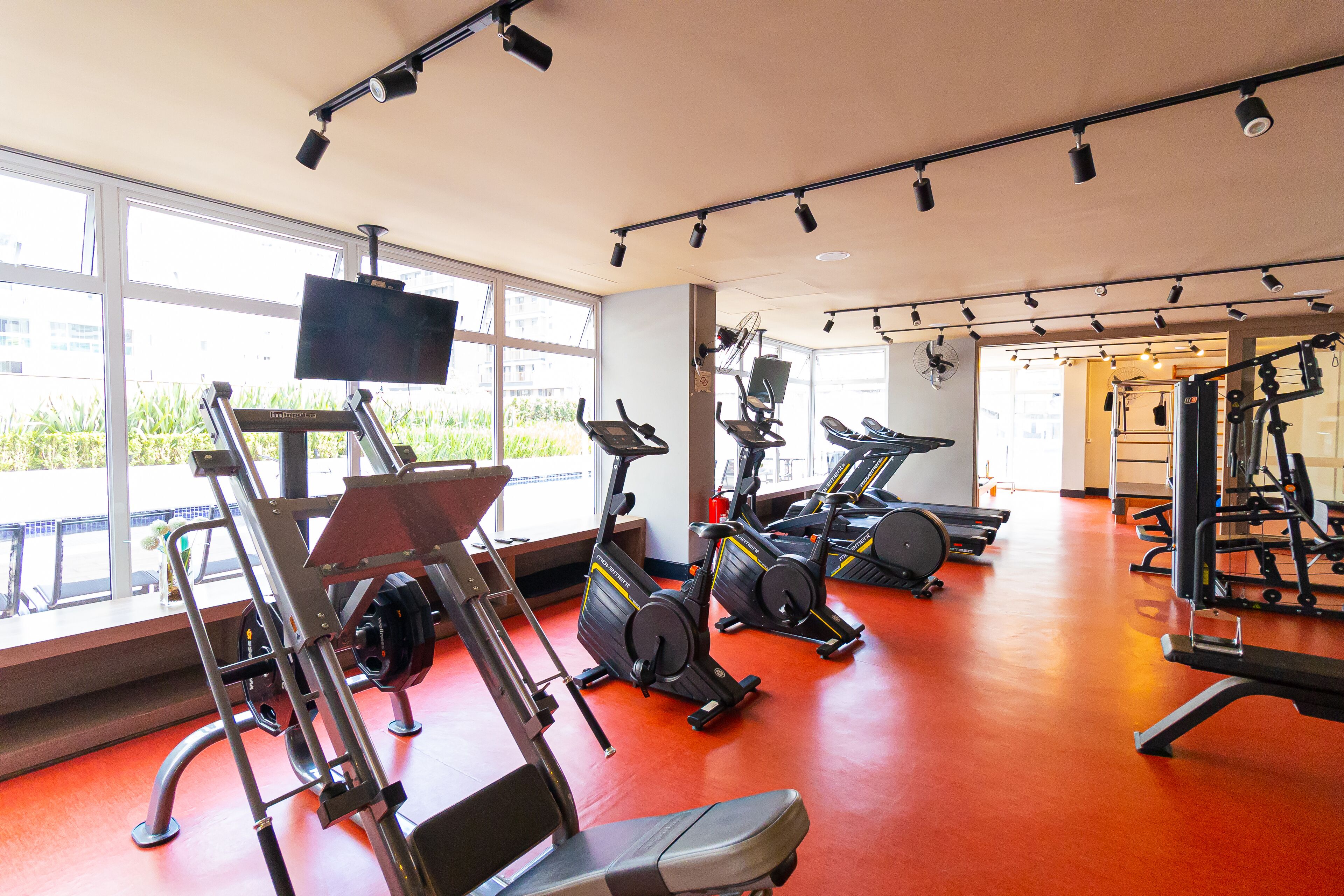 A gym with cardio machines, weightlifting equipment, and large windows.