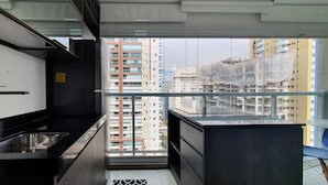 Cocina estrecha con encimera negra, pileta de acero inoxidable y vistas de edificios altos a través de un ventanal grande.