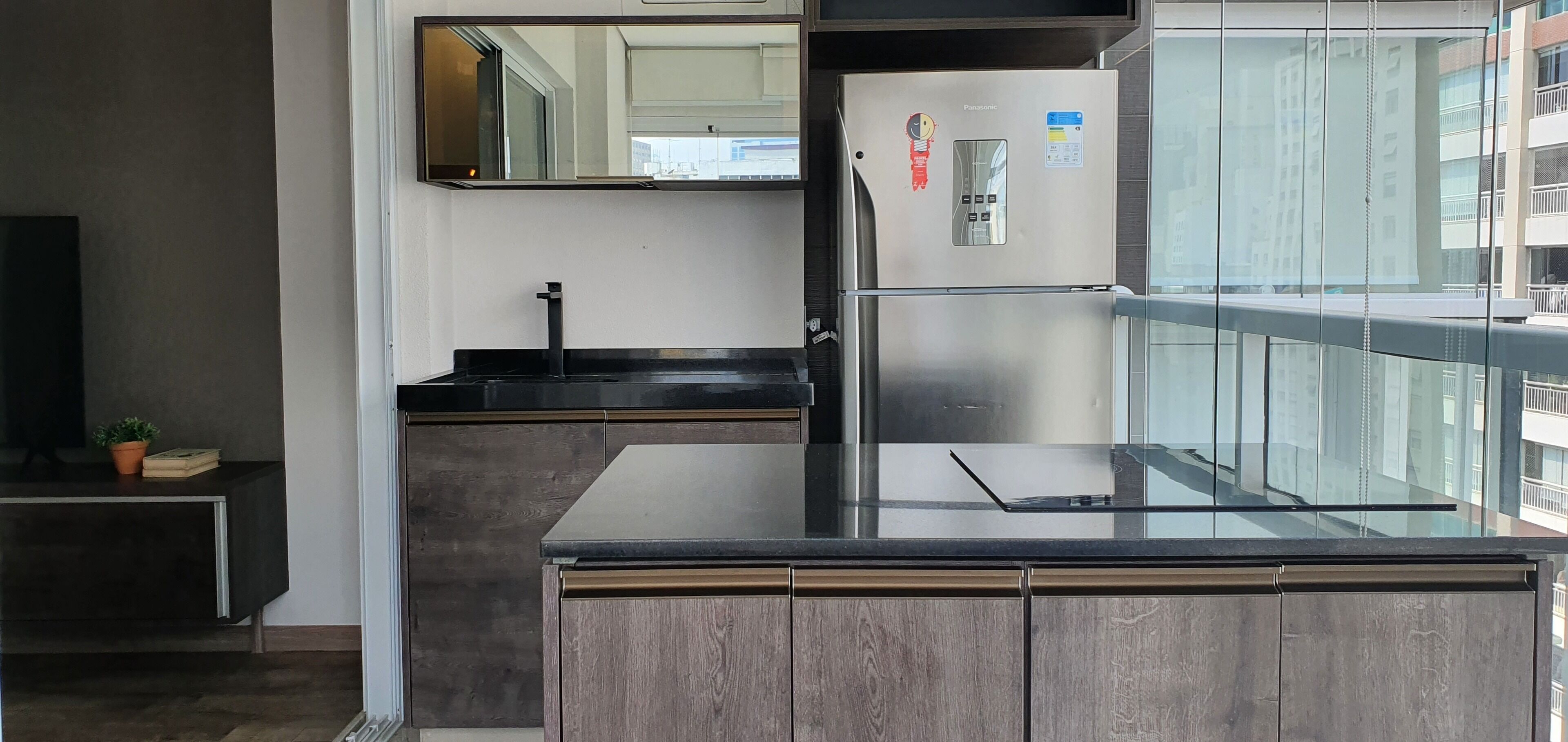 A modern kitchen with a stainless steel refrigerator, a black countertop, and a wooden cabinet.