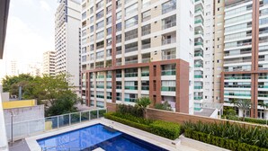 Edificio residencial con piscina en la azotea, rodeado de vegetación y contiguo a edificios de gran altura.