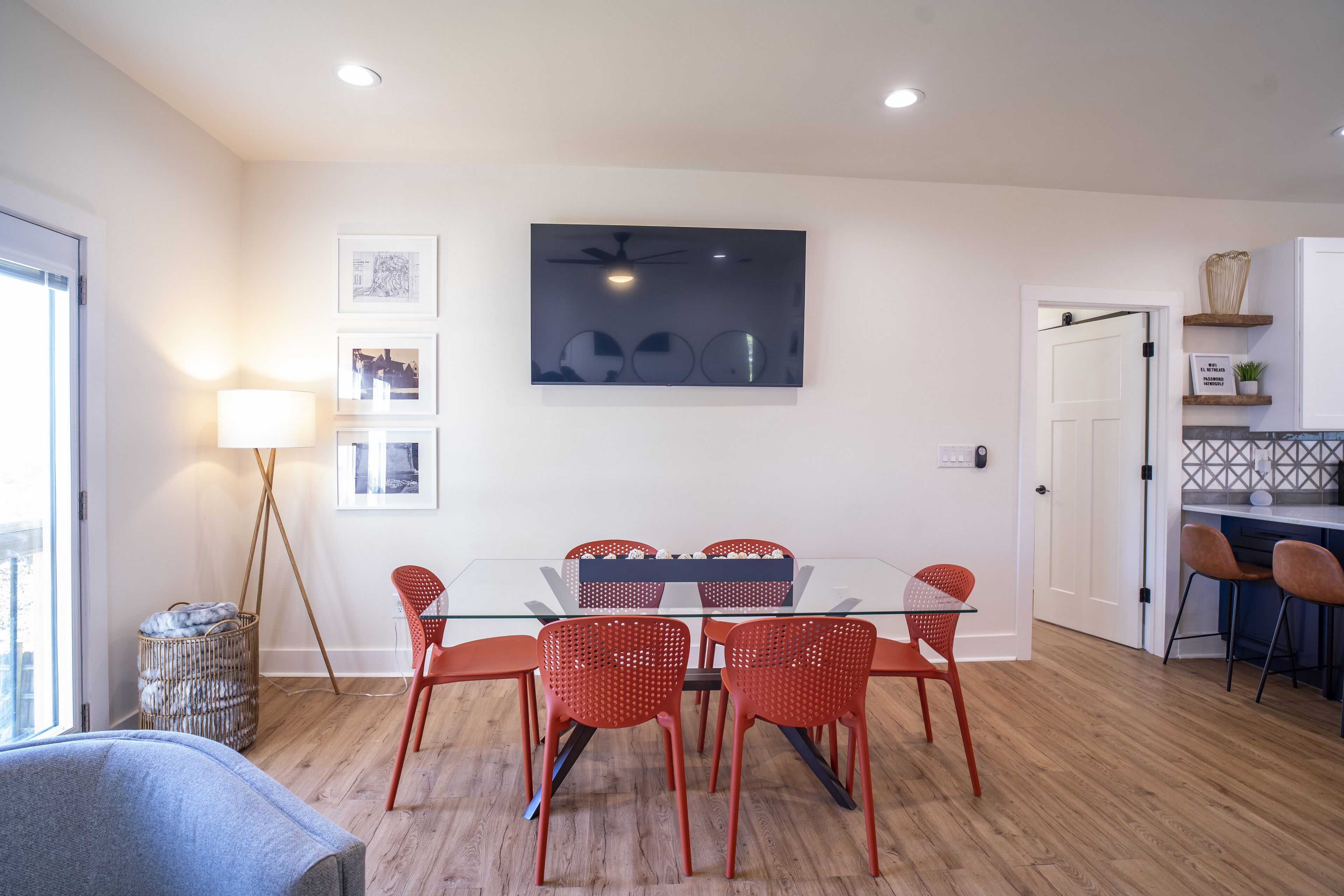 A dining area with a glass table and red chairs, a ceiling fan, and framed pictures on the wall.