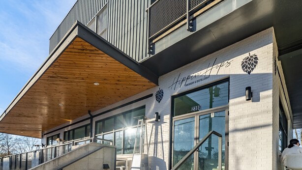 Un edificio moderno con tetto spiovente in legno e ampie finestre, con un cartello che riporta la scritta “Hhippin Brewery & Distillery”.