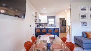 Una cucina moderna con mobili bianchi, un'isola centrale con sgabelli da bar e un'area pranzo con tavolo in vetro e sedie arancioni.
