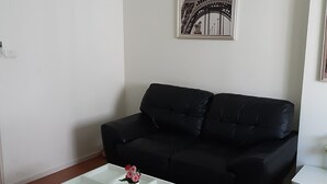 A living room with a black sofa, a glass coffee table with a vase of flowers, and a framed picture on the wall. - Room-t8@impact Challenger Mueang Thon Th (Pak Kret)
