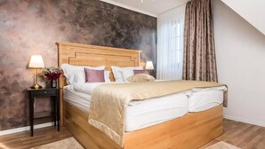 A bedroom with a wooden bed, two bedside tables with lamps, a large window with curtains, and a textured wall. - Soba Deluxe s king size krevetom (Plitvica Selo)