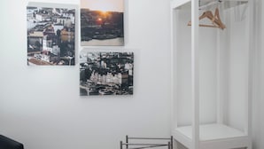A room with three cityscape photographs on the wall, a white wardrobe with a wooden hanger, and a metal stand.