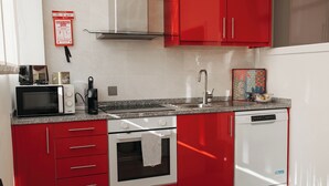 A kitchen with red cabinets, a microwave, an oven, a dishwasher, and a sink.