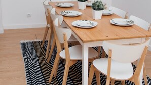 A dining area with a wooden table, white chairs, and a black and white patterned rug.