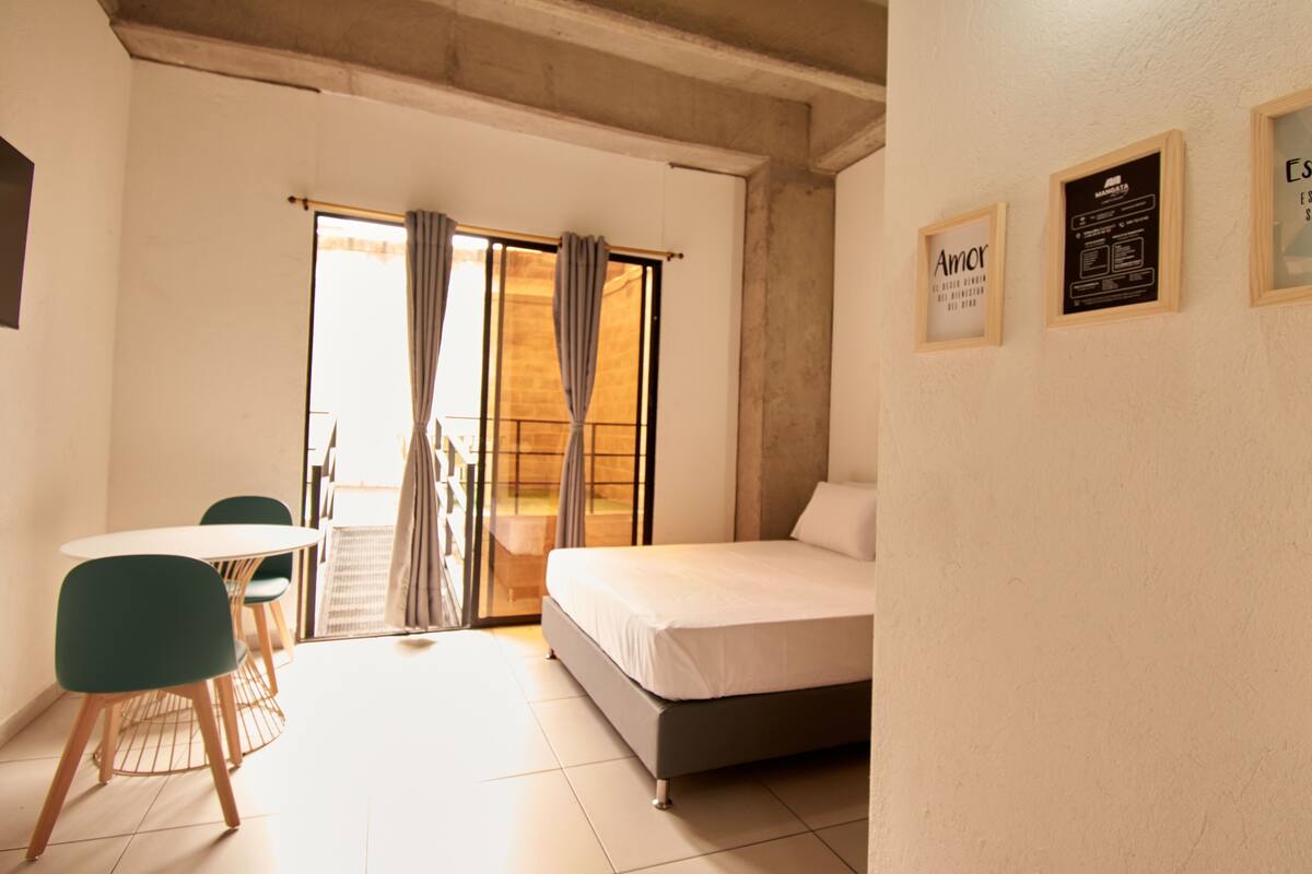 A bedroom with a bed, a table with chairs, and a sliding door leading to a balcony.
