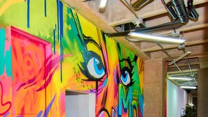 Un mural vibrante y lleno de color con diseños abstractos y ojos grandes en una pared en un espacio interior.