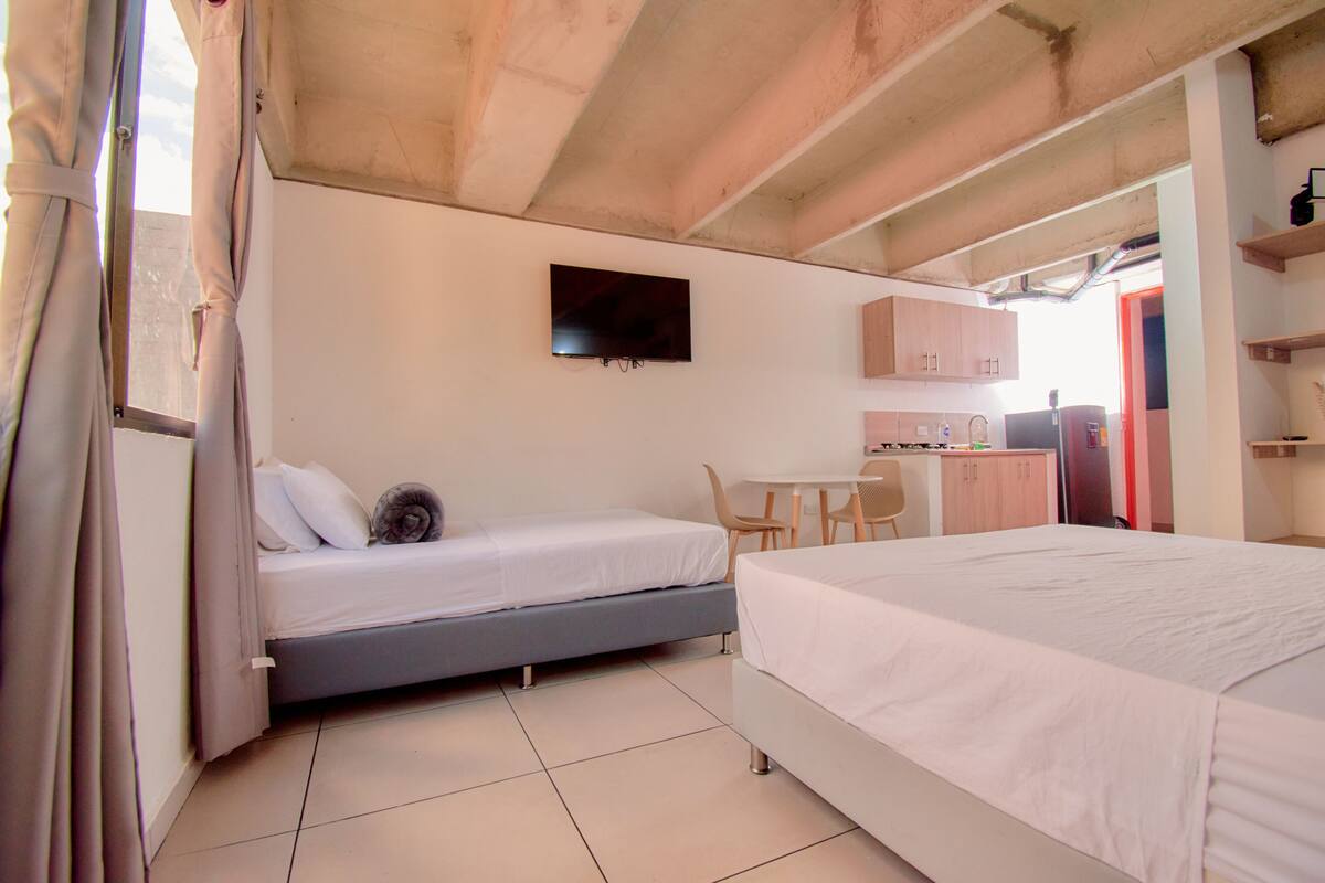 A bedroom with two beds, a TV, a desk, and a kitchenette.