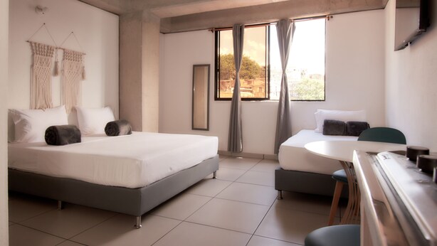 Una habitación de hotel moderna con una cama grande, otra más pequeña, un escritorio y una ventana con cortinas.