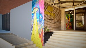 Fachada de un edificio con un mural colorido, una escalera y un muro de ladrillos.