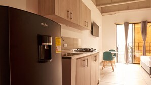 Una cocina moderna con refrigerador empotrado, gabinetes de madera, estufa a gas y un pequeño comedor con una mesa y sillas.