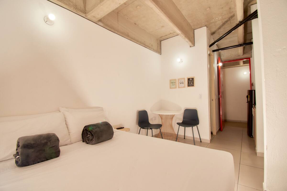 A bedroom with a bed, a small table, two chairs, and a door leading to another room.