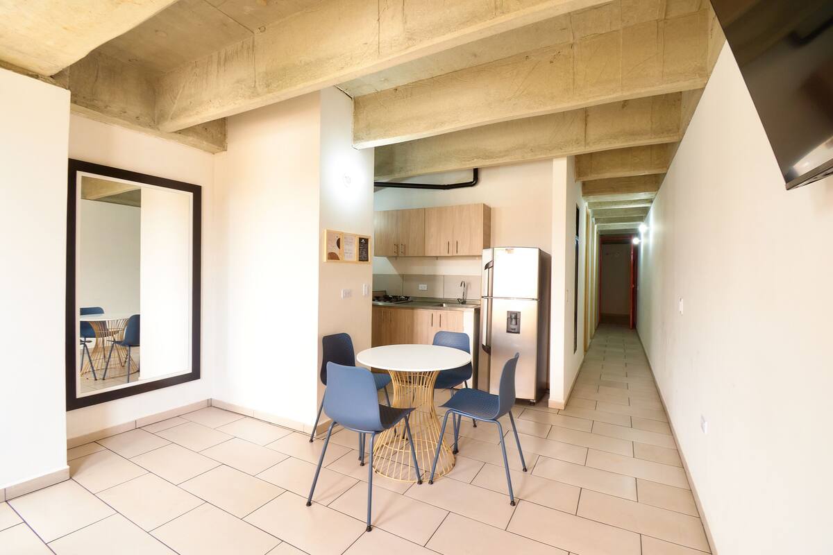 A modern kitchen with a round table and chairs, a refrigerator, and wooden cabinets.