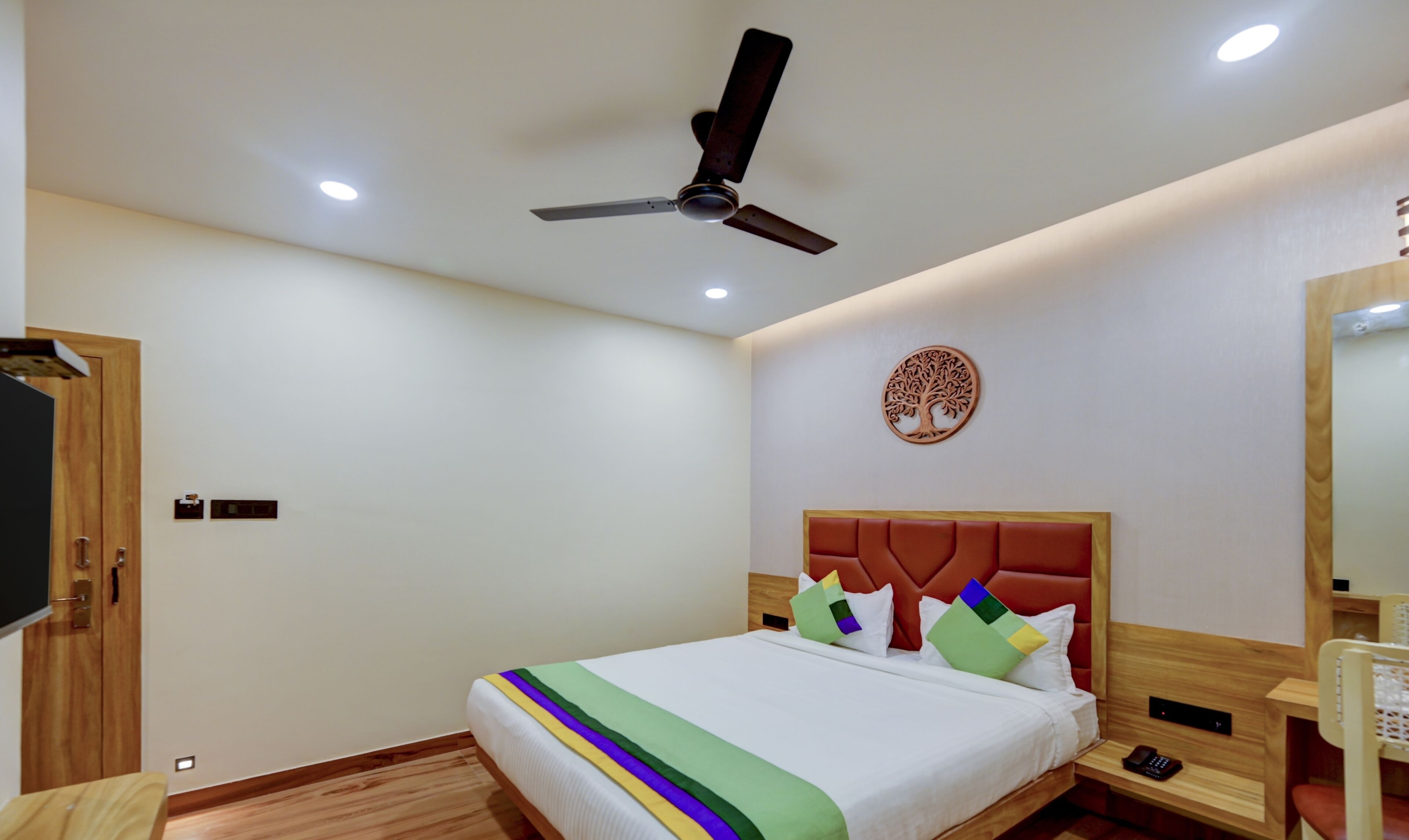 Una habitación de hotel con una cama, un ventilador de techo, un árbol decorativo en la pared y un armario de madera.