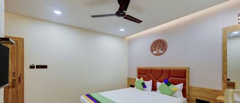 Una habitación de hotel con una cama, un ventilador de techo, un árbol decorativo en la pared y un armario de madera.
