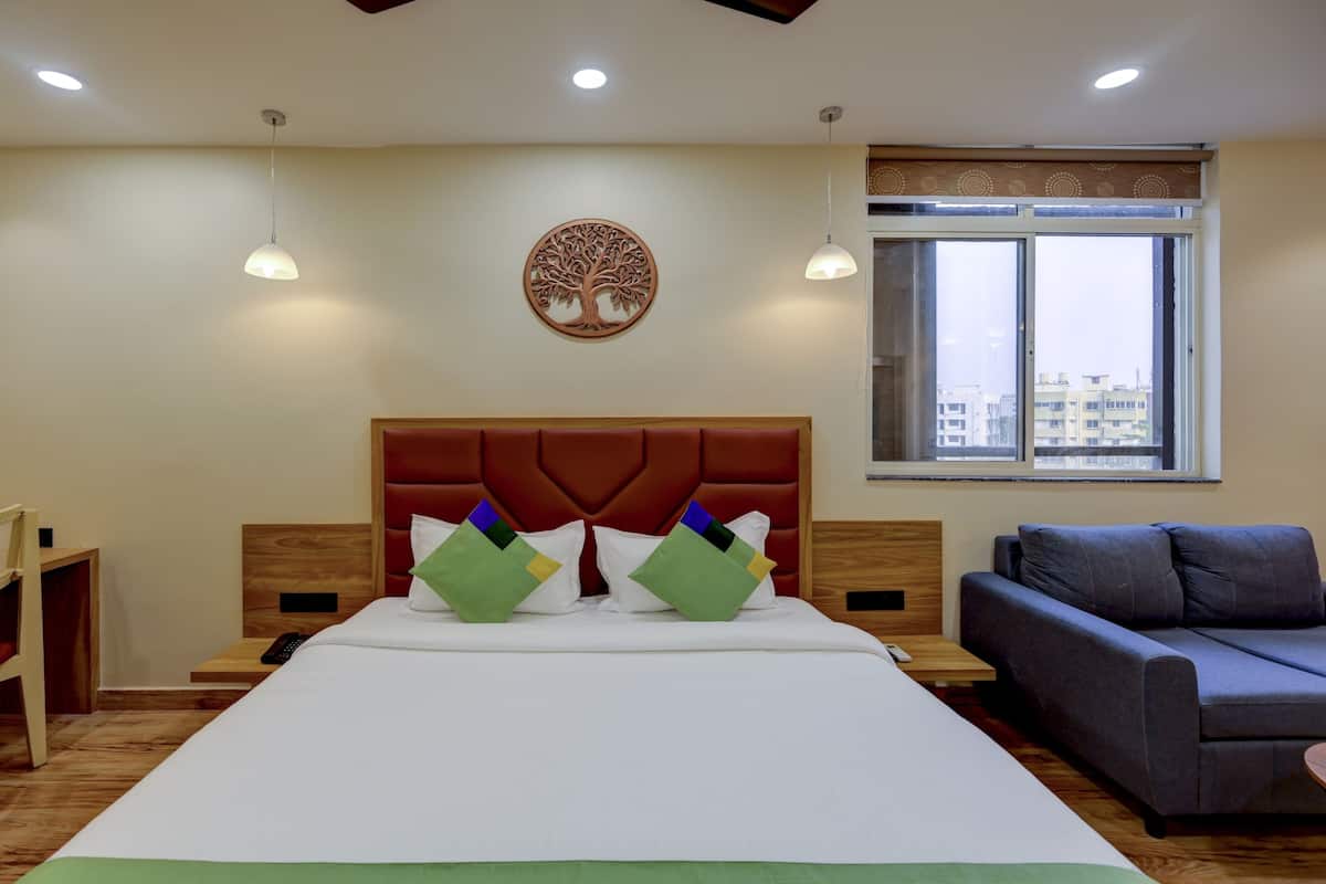 Habitación de hotel con una cama grande, un sofá, un escritorio y una ventana con vista a edificios.