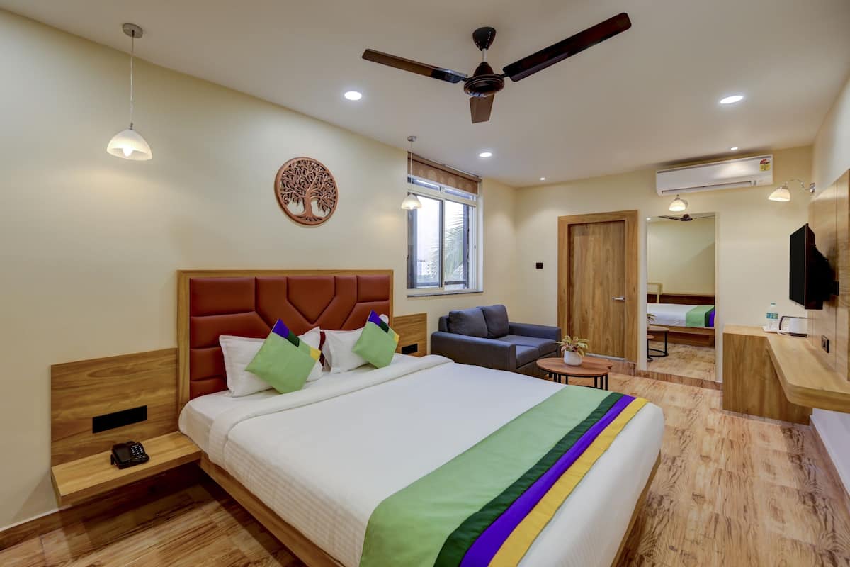 Habitación de hotel con cama, mesita de noche, teléfono, ventilador de techo, ventana y una pequeña zona de estar.