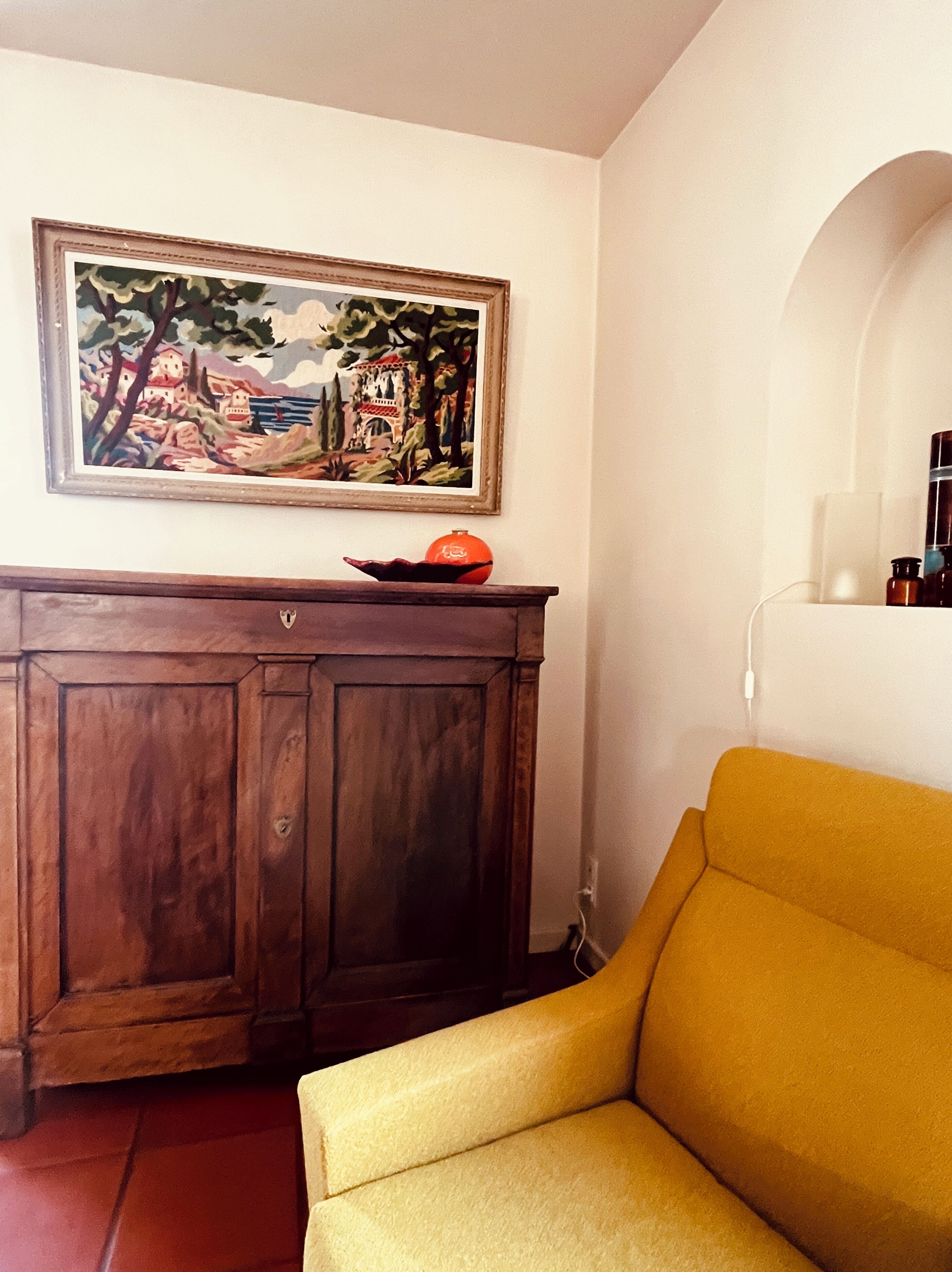 Une pièce avec un meuble en bois, un fauteuil jaune et un tableau accroché au mur.