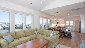 A spacious living room with a large sectional sofa, a wooden coffee table, and a dining area with wooden chairs and a table.