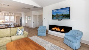 A modern living room with a fireplace, a television mounted above it, and a dining area in the background.