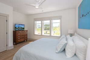 Quarto com cama, penteadeira, TV, janelas e ventilador de teto.