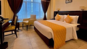 A hotel room with a bed, a desk, a chair, a ceiling fan, and a window with curtains. - Best Western Tirupati Hotel (Tirupati)