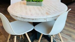 Een ronde eettafel met witte stoelen, een kroonluchter erboven en een keuken in de achtergrond.