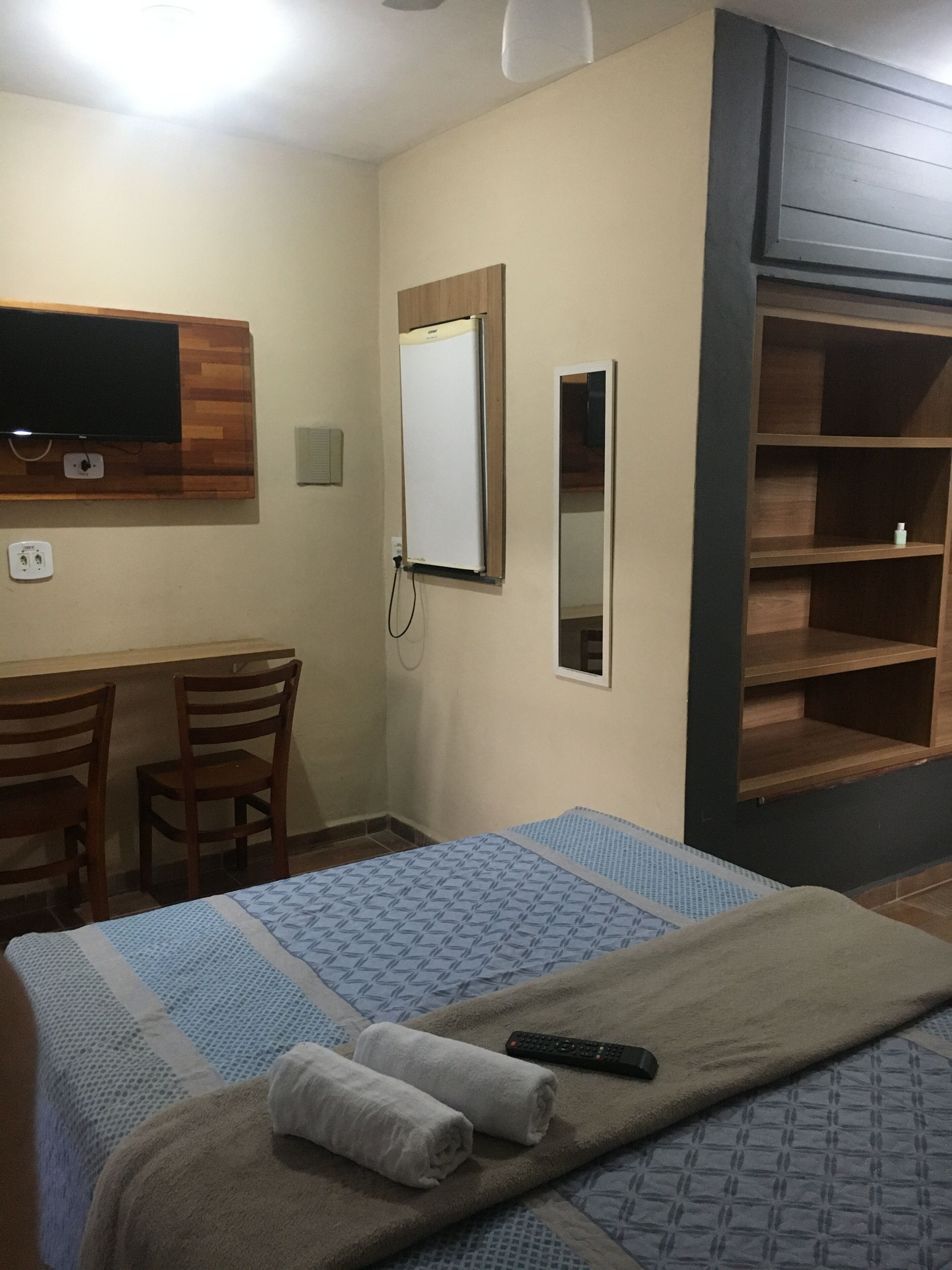 Habitación de hotel con cama, escritorio, silla, televisor montado en un panel de madera y espejo.