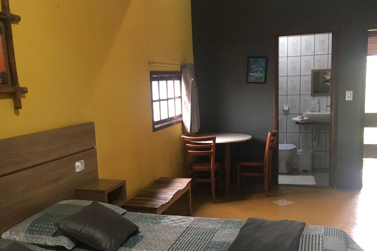 Quarto com cama, escrivaninha e banheiro.
