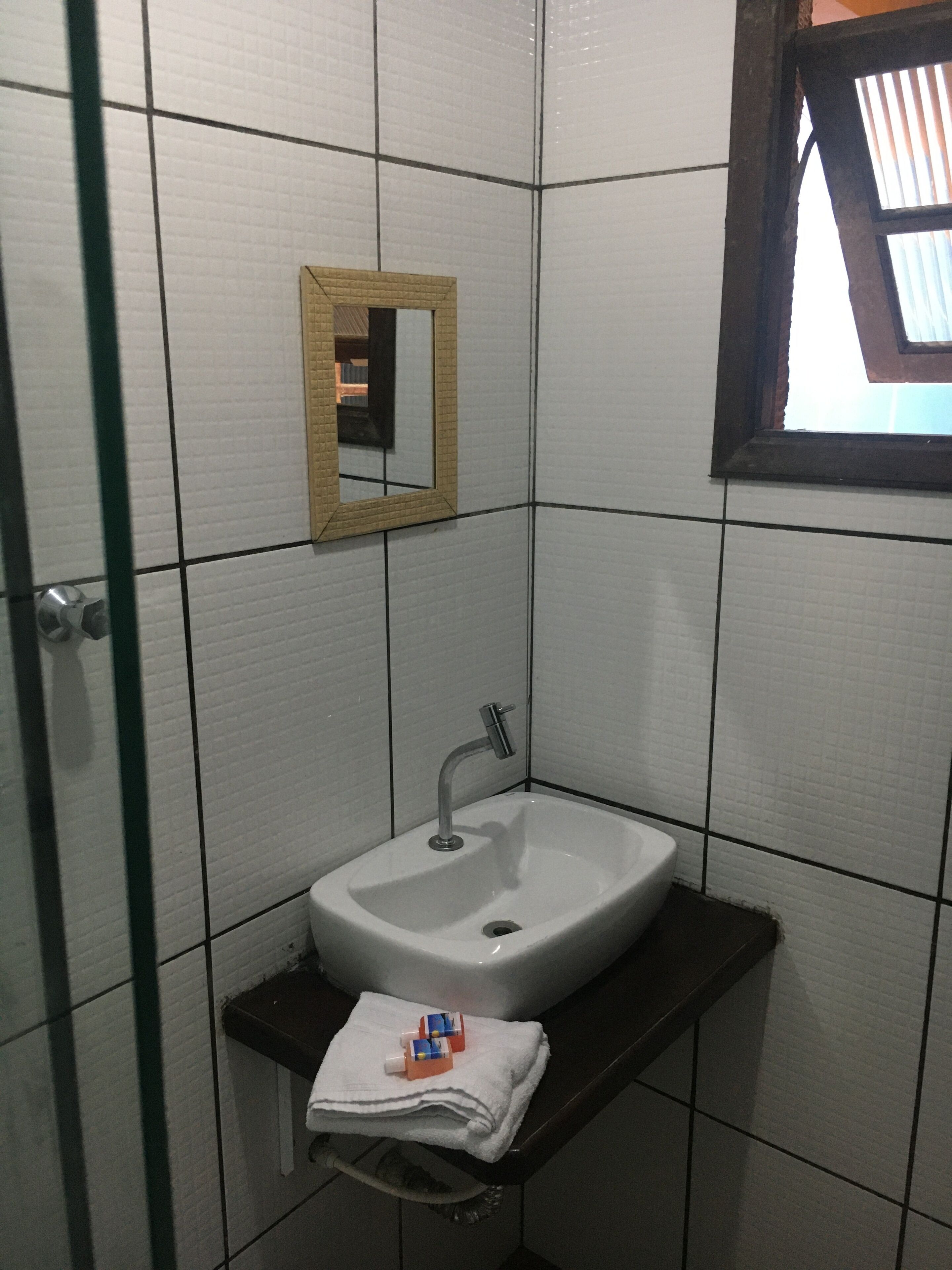 A bathroom with white tiled walls, a white sink with a single faucet, a small mirror, and a towel on a shelf.