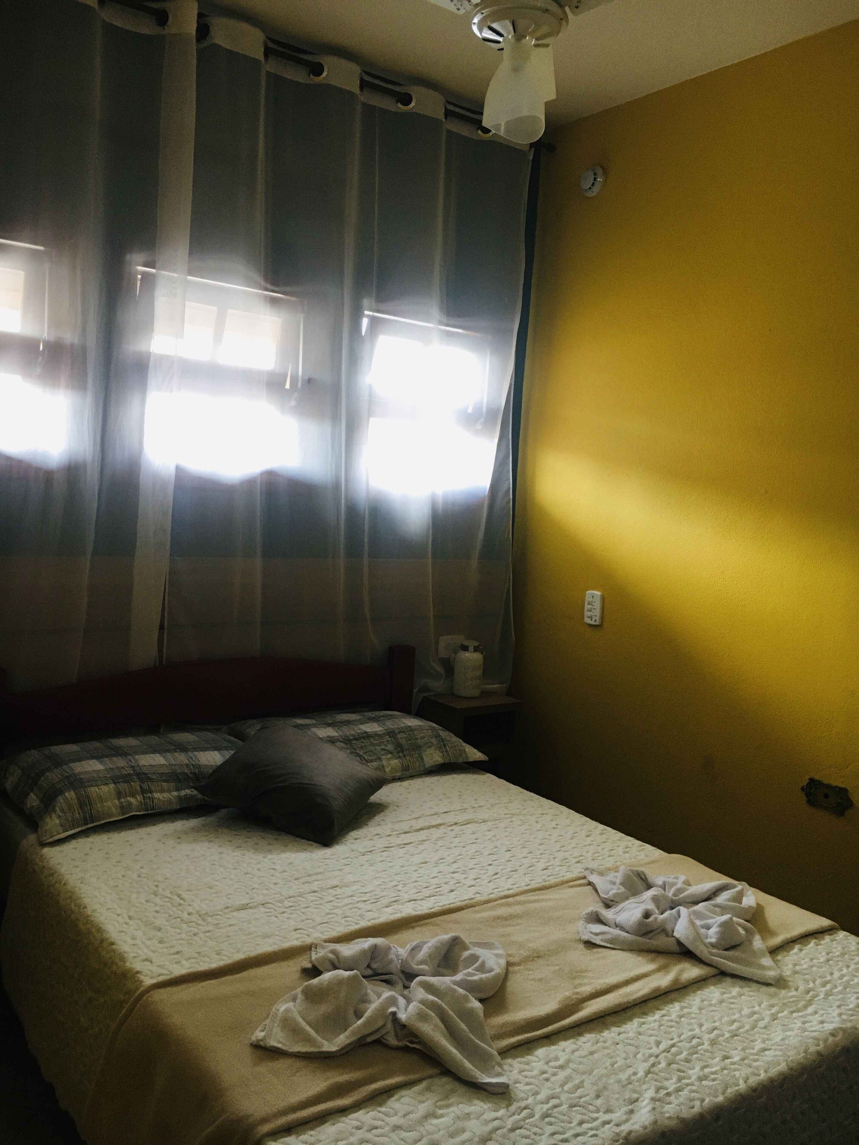 A hotel room with a bed, curtains, a bedside table, and a wall clock.