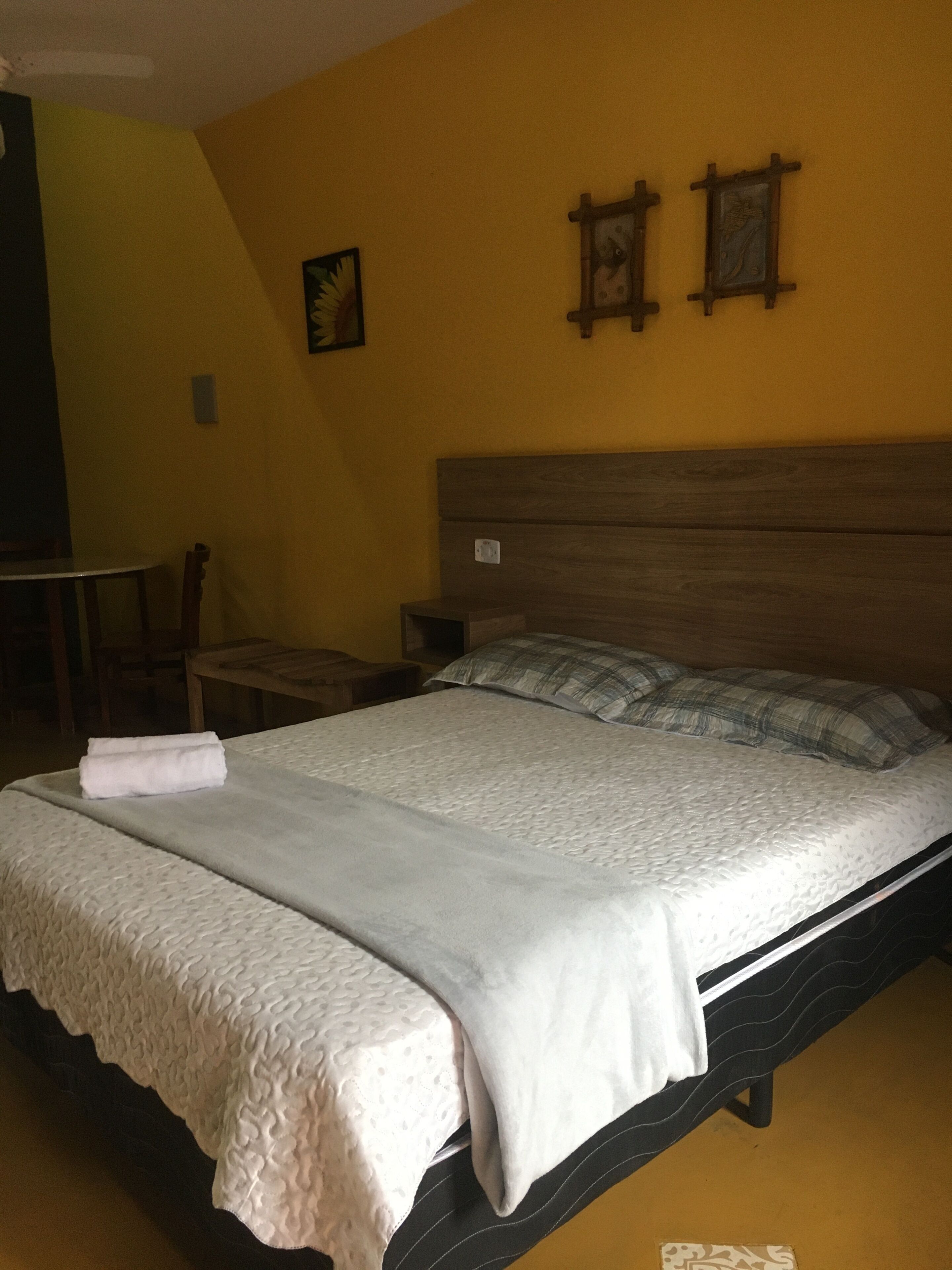 Een bed met een witte dekbedovertrek en kussens, een houten hoofdbord en een klein nachtkastje.