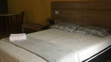 Een bed met een witte dekbedovertrek en kussens, een houten hoofdbord en een klein nachtkastje.
