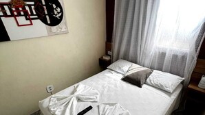 Een enkel bed met witte beddengoed, een afstandsbediening en een decoratieve handdoek op het bed.
