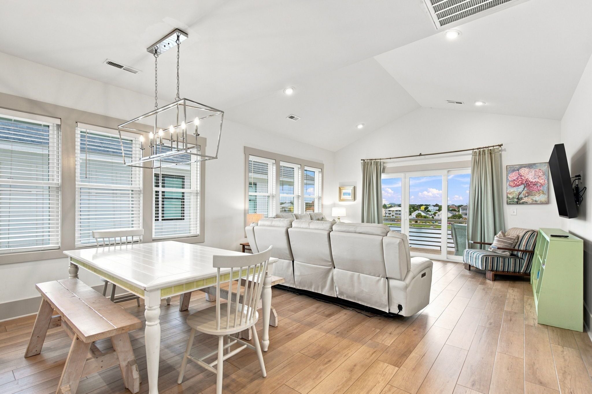 Amplia sala de estar con sofá blanco, mesa de comedor con sillas y un ventanal con vistas al exterior.