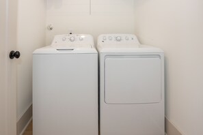 Two white front-loading washing machines in a laundry room with a door on the left.