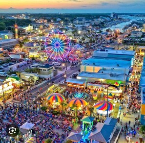 A bustling outdoor market with a Ferris wheel and colorful umbrellas.