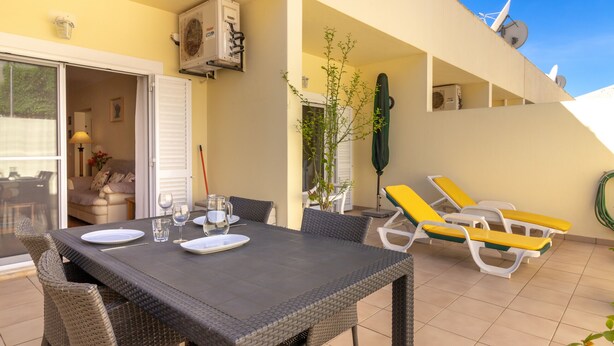 An outdoor dining area with a table and chairs, a plant, and a view of the interior. - Casa Amiga - Communal pool & garden, just 500m from beach (Carvoeiro)