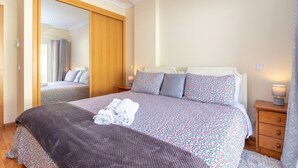 A bedroom with a large bed, a wardrobe, a bedside table with a lamp, and a mirror. - Casa Amiga - Communal pool & garden, just 500m from beach (Carvoeiro)